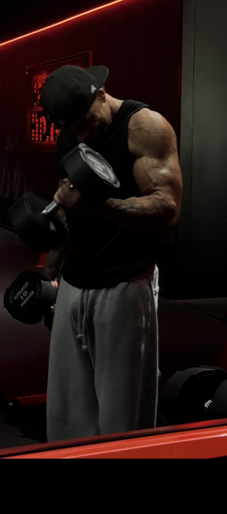 Le coach en plein curl biceps, concentré, dans la salle en pénombre